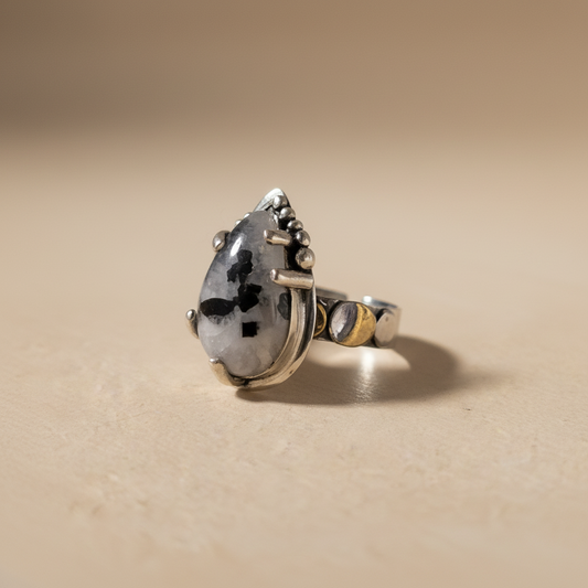 Silver ring with a large teardrop-shaped gemstone on a beige background