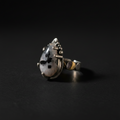 A silver ring featuring a teardrop-shaped white stone with black speckles, set against a dark black background.