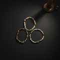 Three beaded stretch bracelets arranged in a triangle on a dark surface, with a bronze candle holder partially visible in the top right corner.