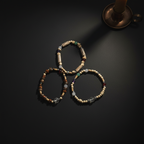 Three beaded stretch bracelets arranged in a triangle on a dark surface, with a bronze candle holder partially visible in the top right corner.