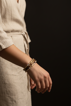 A close-up of a person's wrist wearing multiple beaded bracelets, including a dark brown beaded bracelet and a gold-toned beaded bracelet, against a dark background.