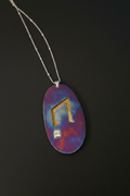 A silver-toned necklace with an oval pendant featuring a blue and purple marbled background, a gold-colored musical note, and a small white cube charm, shown against a dark background.
