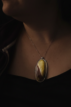 A close-up lifestyle shot of a person wearing a silver-toned chain necklace with an oval pendant featuring a marbled yellow, brown, and dark brown stone.