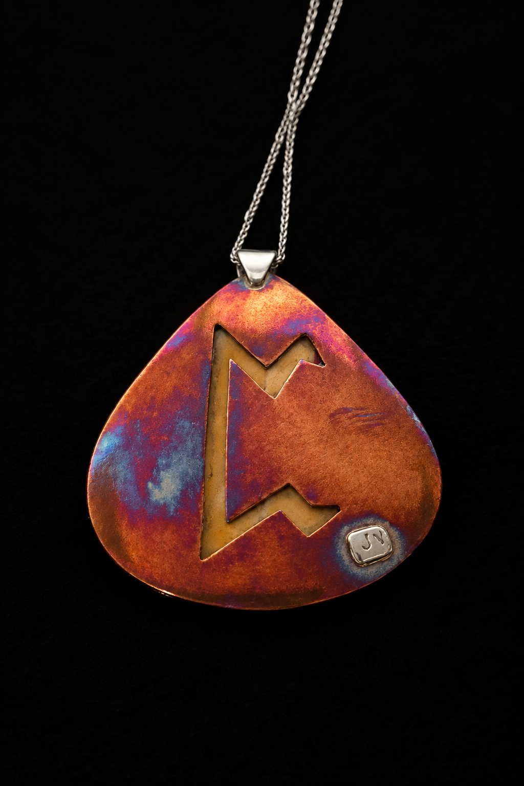 A teardrop-shaped pendant necklace with a cutout Norse letter 'M' design, featuring a textured copper and purple iridescent finish, suspended on a black background.