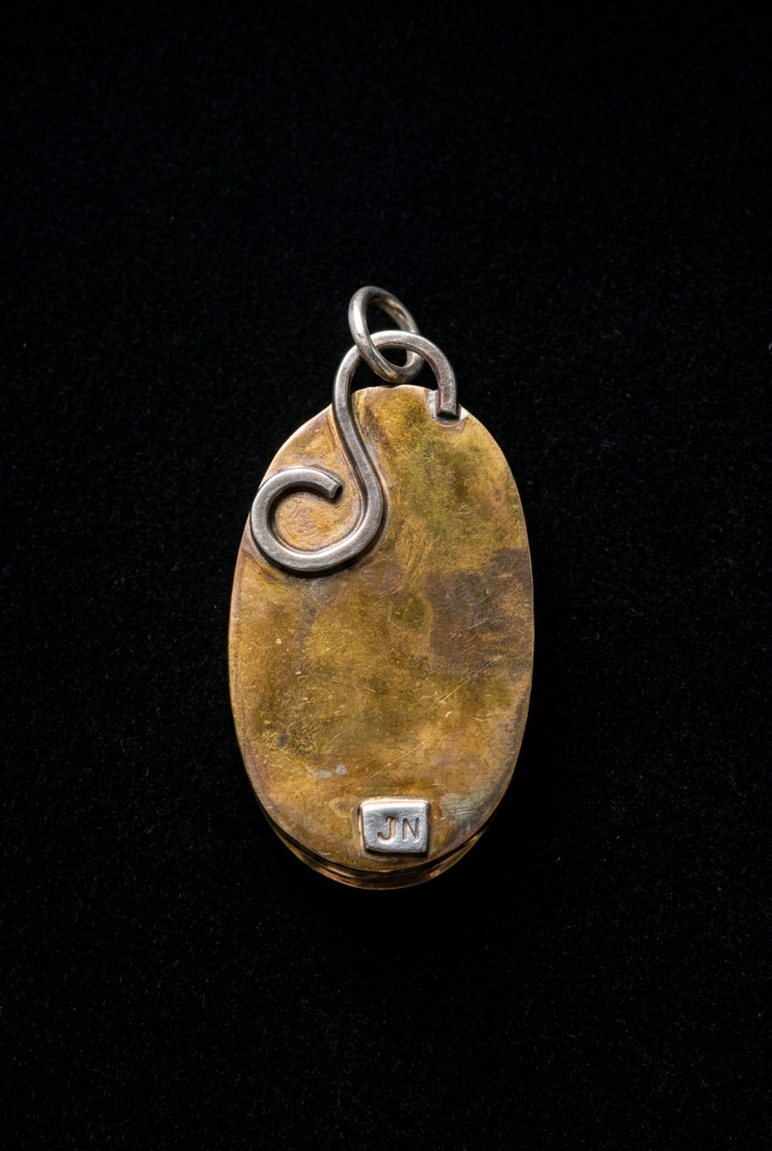 A vintage oval pendant with a warm gold-toned center and a silver-toned bail featuring a stylized swirl, shown on a dark gray background.