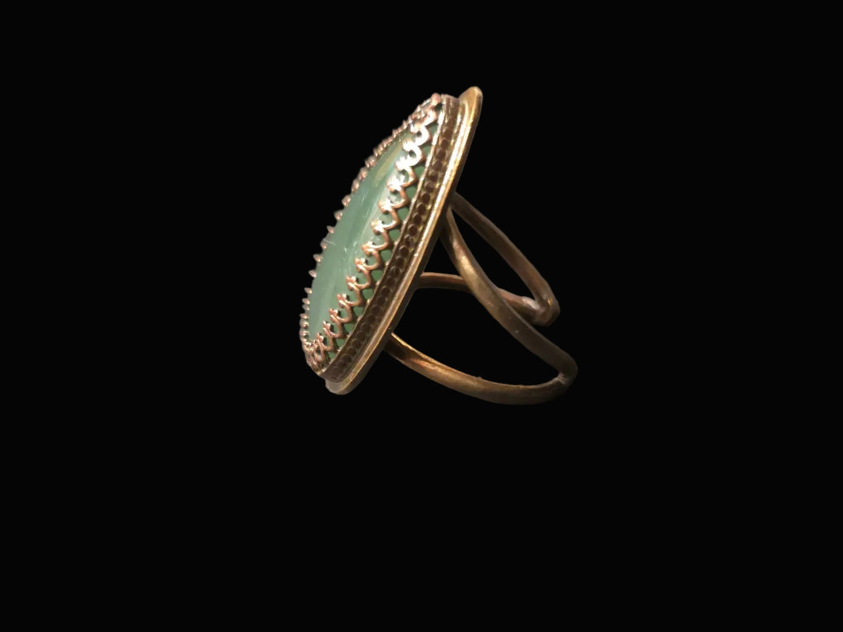 A gold ring with a large oval light green stone, set against a solid black background.