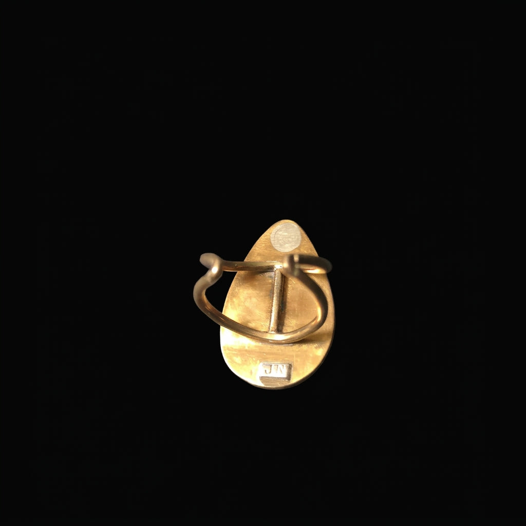 A small gold-toned jewelry piece, possibly a ring or pendant, shown against a solid black background.
