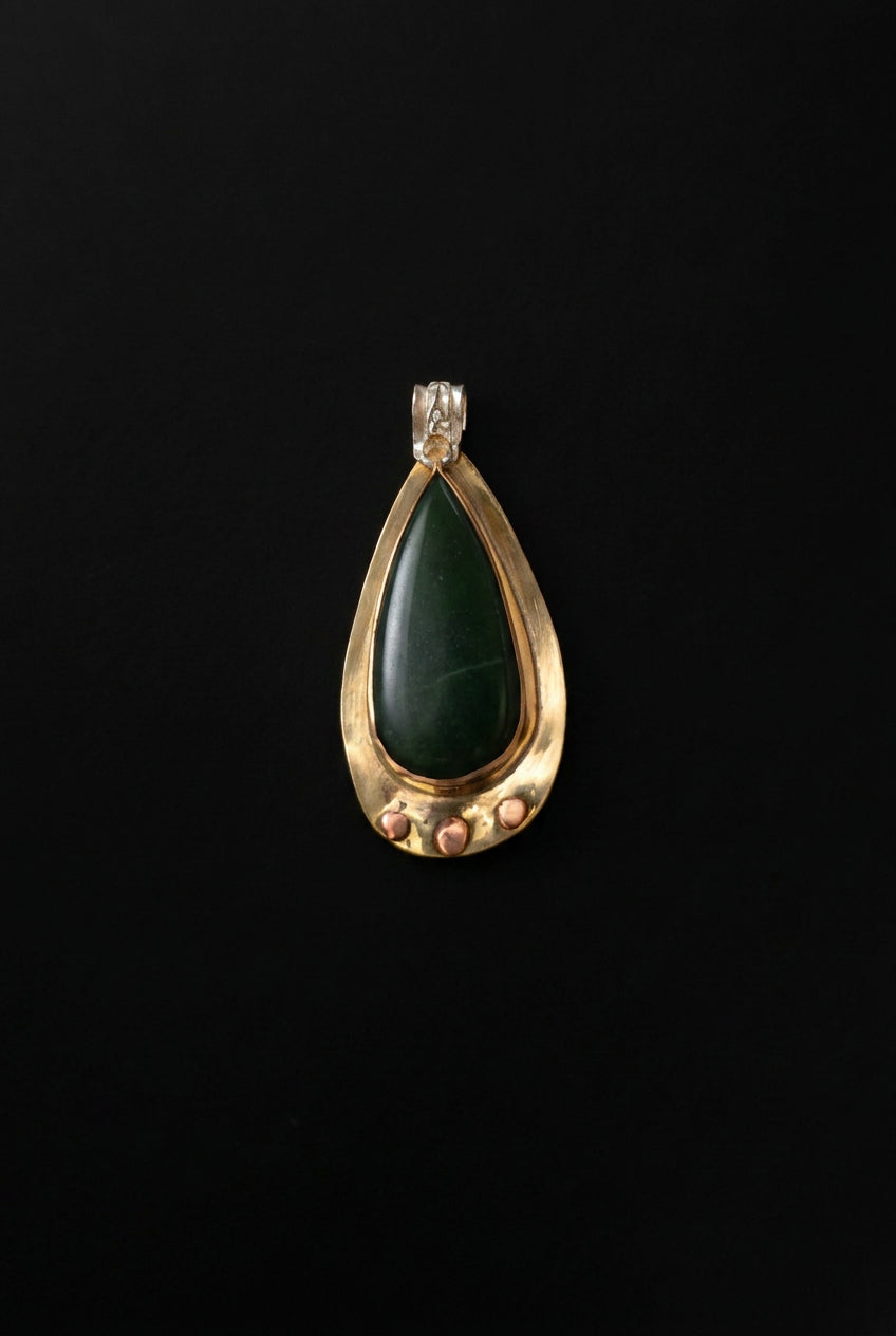 A teardrop-shaped pendant featuring a dark green stone in a gold-toned setting with a clear crystal bail, displayed on a dark background.