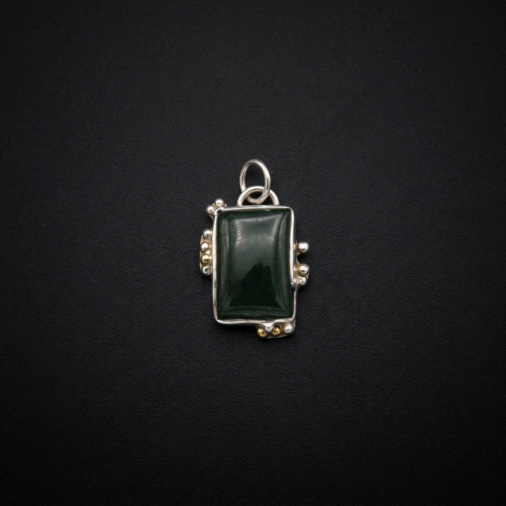 A silver-toned rectangular pendant or brooch featuring a dark green cabochon gemstone, displayed on a dark gray surface.
