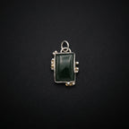 A silver-toned rectangular pendant or brooch featuring a dark green cabochon gemstone, displayed on a dark gray surface.