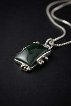 A small silver-toned ring with a dark green rectangular stone, photographed on a dark gray textured surface.