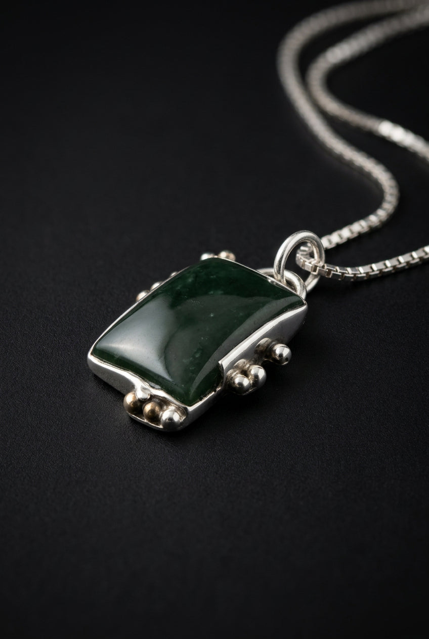 A small silver-toned ring with a dark green rectangular stone, photographed on a dark gray textured surface.