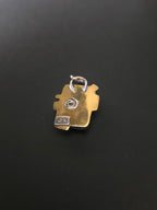 A small gold-toned pendant or charm with a silver ring attachment, photographed on a dark black surface.
