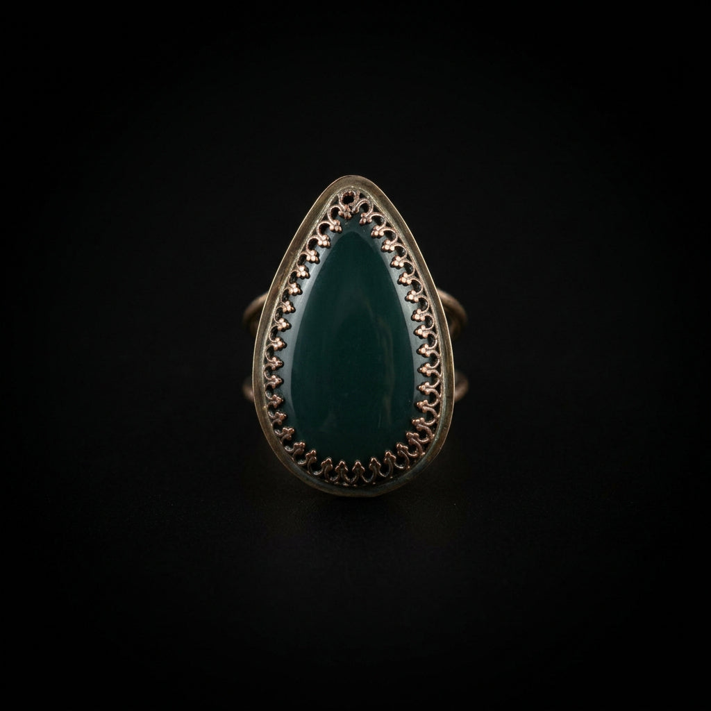A teardrop-shaped ring with a dark green stone and a dark metal bezel setting, resting on a textured white paper towel.
