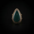 A teardrop-shaped ring with a dark green stone and a dark metal bezel setting, resting on a textured white paper towel.