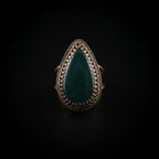 A teardrop-shaped ring with a dark green stone and a dark metal bezel setting, resting on a textured white paper towel.