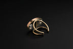 A small metallic ring or clasp with a silver-toned band and gold-toned end, resting on a white paper towel over a blurred desk background.
