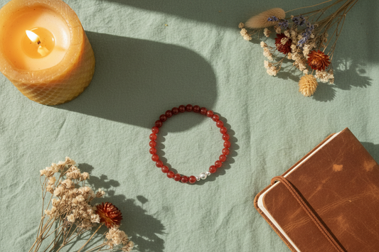 Red beaded bracelet on a light green surface with a lit candle and dried flowers.