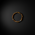 A beaded bracelet made of round brown and gold tiger's eye beads with a small silver spacer bead, displayed on a dark textured background.
