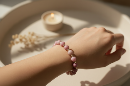Hand wearing a pink beaded bracelet with a softly lit candle in the background
