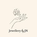 Logo of 'Jewellery by JN' featuring a hand holding crystals on a beige background.