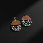 A pair of handmade dangle earrings on a dark textured background. Each earring features a semi-circular wooden top engraved with 'LOVE' and adorned with multiple strands of small multicolored seed beads hanging below.