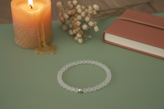 Flat lay of Lumenveil Bracelet with translucent matte clear quartz and a central silver accent bead, handmade ritual jewellery.