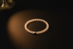 A beaded stretch bracelet made of translucent pale pinkish-beige round beads, with a small metallic silver accent bead, displayed on a dark surface under warm spotlighting.