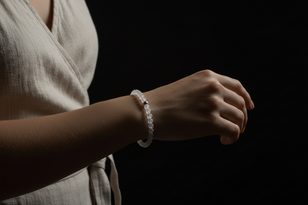 A person wearing a white beaded bracelet on their wrist, shown from the chest down against a solid black background.