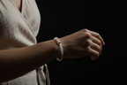 A person wearing a white beaded bracelet on their wrist, shown from the chest down against a solid black background.