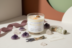 Manifestation Intention Candle by Jewellery by JN, hand-poured candle with Clear Quartz and Tiger's Eye crystals, sage, and silver and gold shimmer, displayed on creamy linen with ritual props.