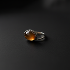 A silver ring with an oval amber-brown cabochon gemstone, photographed on a dark textured surface.