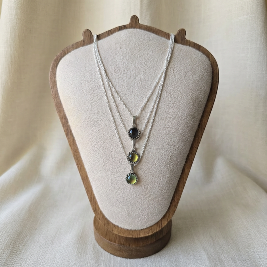Necklace with three pendant stones on a wooden bust against a beige background