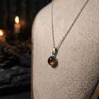 Necklace with a pendant on a mannequin bust against a dark background with candles.
