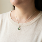 Person wearing a necklace with a green pendant on a plain background