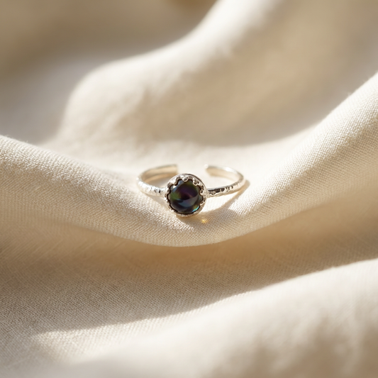 Silver ring with a dark gemstone on a beige fabric background