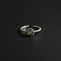 A silver adjustable ring featuring a central oval-cut iridescent stone with blue and green flashes, set on a textured dark background.