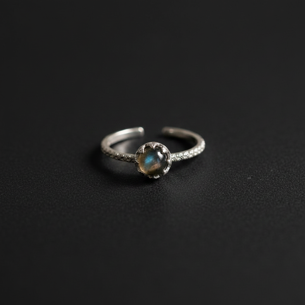 A silver adjustable ring featuring a central oval-cut iridescent stone with blue and green flashes, set on a textured dark background.