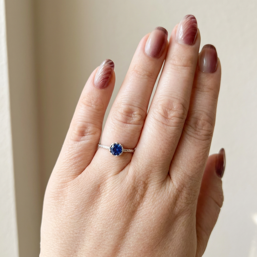 Hand wearing a ring with a blue gemstone on a neutral background