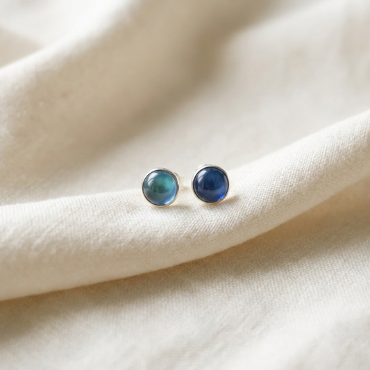 Pair of blue gemstone stud earrings on a beige fabric background
