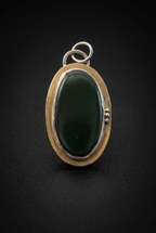 Handcrafted oval green aventurine pendant featuring a smooth cabochon gemstone set in a patinated brass bezel frame with silver accent beads and top bail loop resting on a dark moody surface.