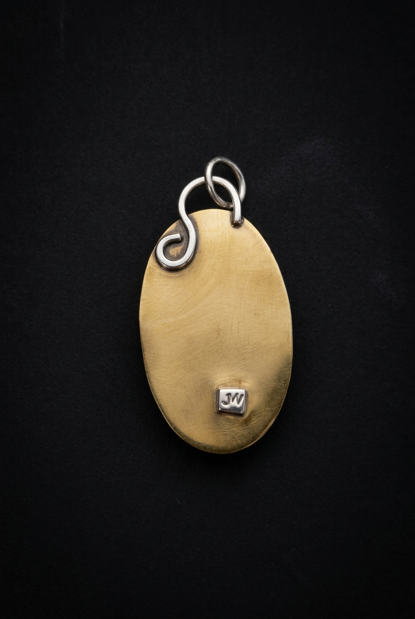 Back view of a handcrafted brass oval pendant showcasing a smooth patinated brass surface, intricate wire bail loop, and stamped maker's hallmark on a dark background.