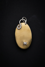 Back view of a handcrafted brass oval pendant showcasing a smooth patinated brass surface, intricate wire bail loop, and stamped maker's hallmark on a dark background.