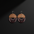A pair of handmade dangle earrings on a dark background. Each earring features a semi-circular wooden top piece engraved with 'LOVE IS' and three cascading strands of small beads in shades of burgundy, purple, and dark brown, suspended from silver-tone fishhook wires.