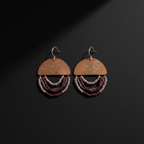 A pair of handmade dangle earrings on a dark background. Each earring features a semi-circular wooden top piece engraved with 'LOVE IS' and three cascading strands of small beads in shades of burgundy, purple, and dark brown, suspended from silver-tone fishhook wires.
