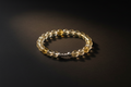 A beaded stretch bracelet made of faceted clear and golden-yellow beads with a small silver spacer, photographed on a dark black background.