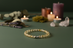 Yellow beaded bracelet on a dark green surface with candles and crystals in the background