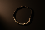 A beaded bracelet with dark brown and white beads separated by small gold spacer beads, displayed on a dark background.