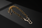 A gold chain bracelet with a unique pendant featuring three interlocking circular cutouts, displayed on a dark textured surface.