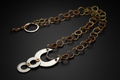 A handmade link chain necklace featuring alternating bronze and gold-toned metal rings, with a central silver crescent moon and disc pendant accented by small gold and purple details, displayed on a dark background.